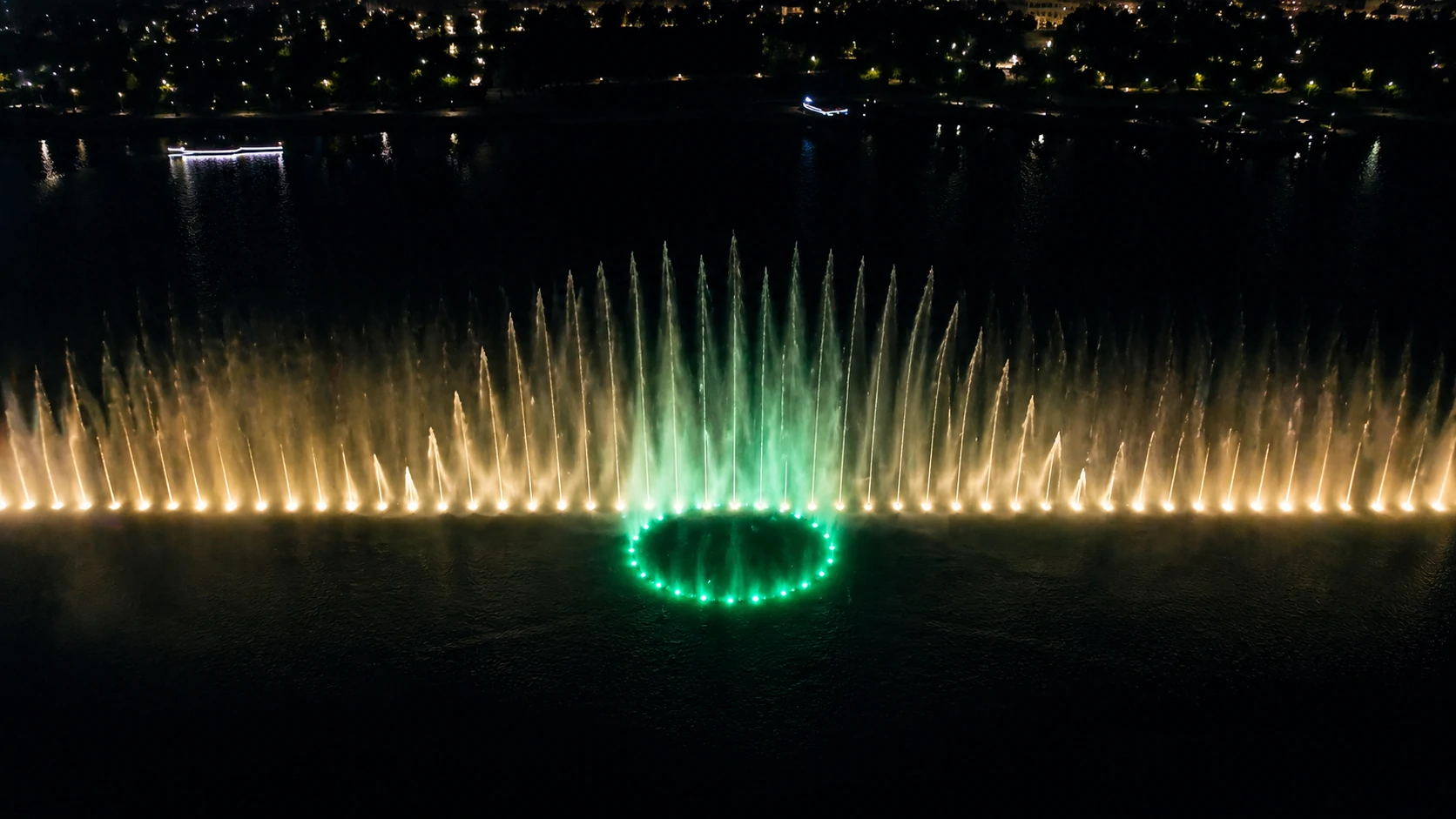 Lake dancing fountain night show with large-scale water jets and lighting effects on a waterfront site