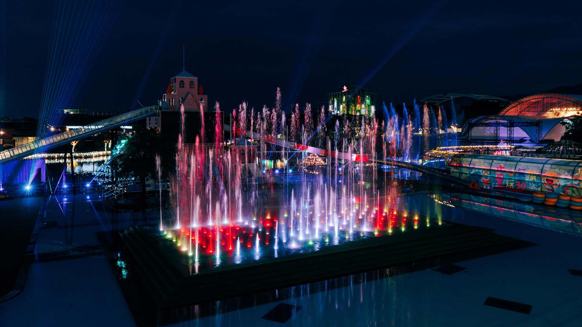 Large dry deck fountain night show in a public plaza with ground-level water jets and lighting